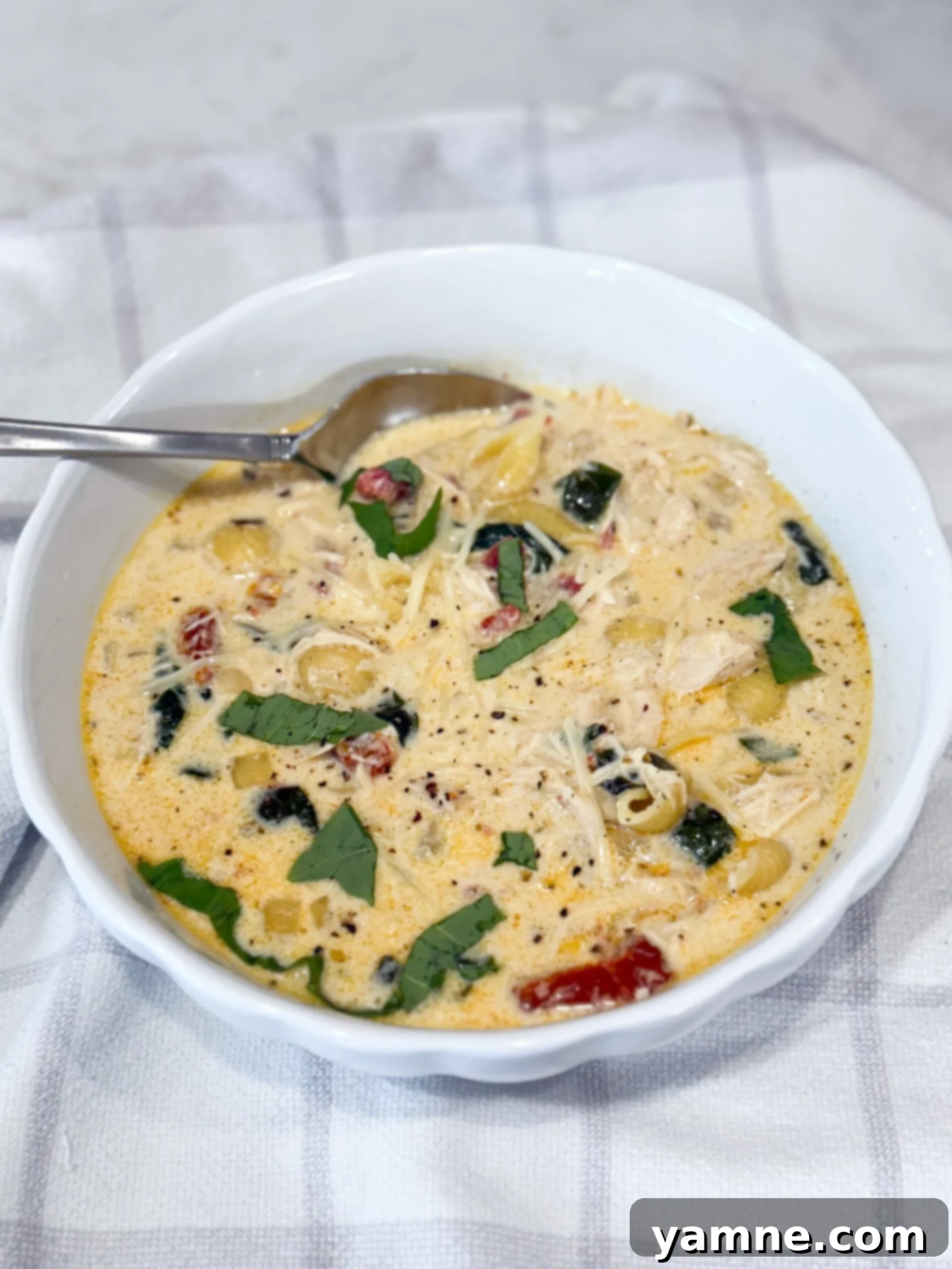 A steaming bowl of Slow Cooker Marry Me Chicken Soup filled with pasta, spinach, and a generous sprinkle of Parmesan cheese.
