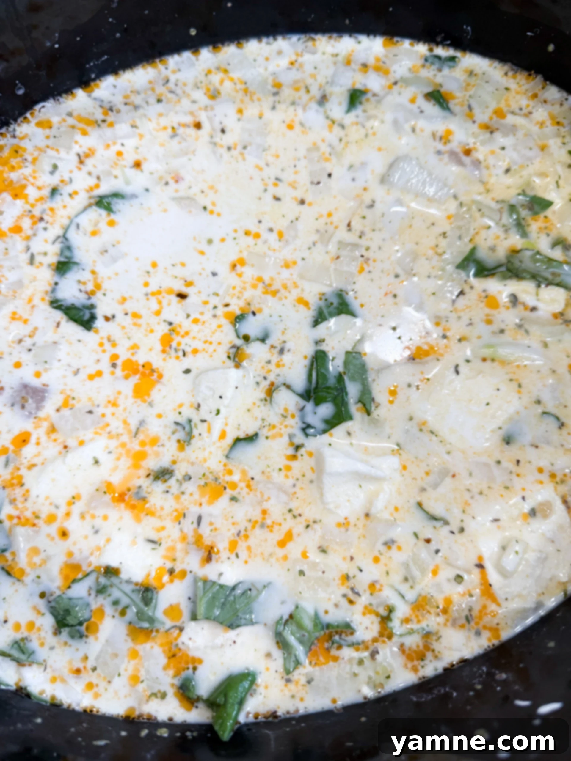 Chicken, cream cheese, chicken broth, and fresh basil in a slow cooker ready to be cooked.