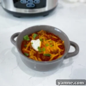 A steaming bowl of Slow Cooker Chili, topped with a generous sprinkle of shredded cheese and fresh green onions.