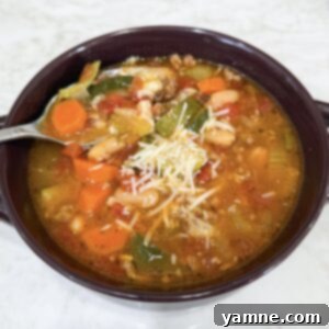 A vibrant bowl of Slow Cooker Italian Vegetable and Sausage Soup, generously topped with grated Parmesan cheese and fresh herbs.