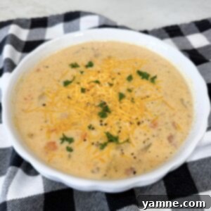 A bowl of rich, creamy Slow Cooker Ham and Potato Soup, garnished with shredded cheddar cheese and a sprig of fresh parsley.