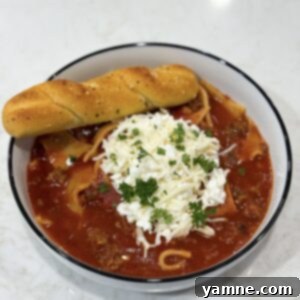 A hearty bowl of slow cooker lasagna soup, garnished with a spoonful of creamy ricotta, fresh basil, and a rustic spoon.