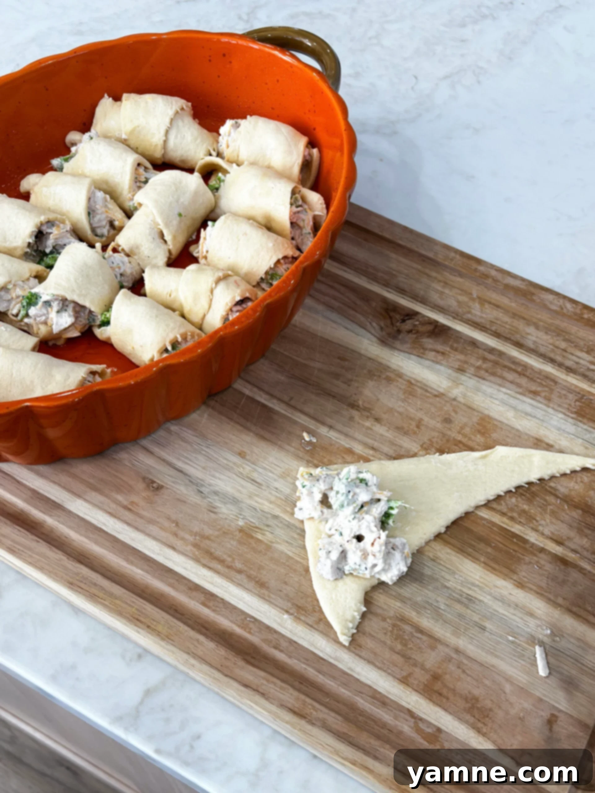Flaky Cheesy Chicken and Broccoli Bake 6 Rolling the creamy chicken and broccoli mixture into crescent dough triangles, ready for baking.