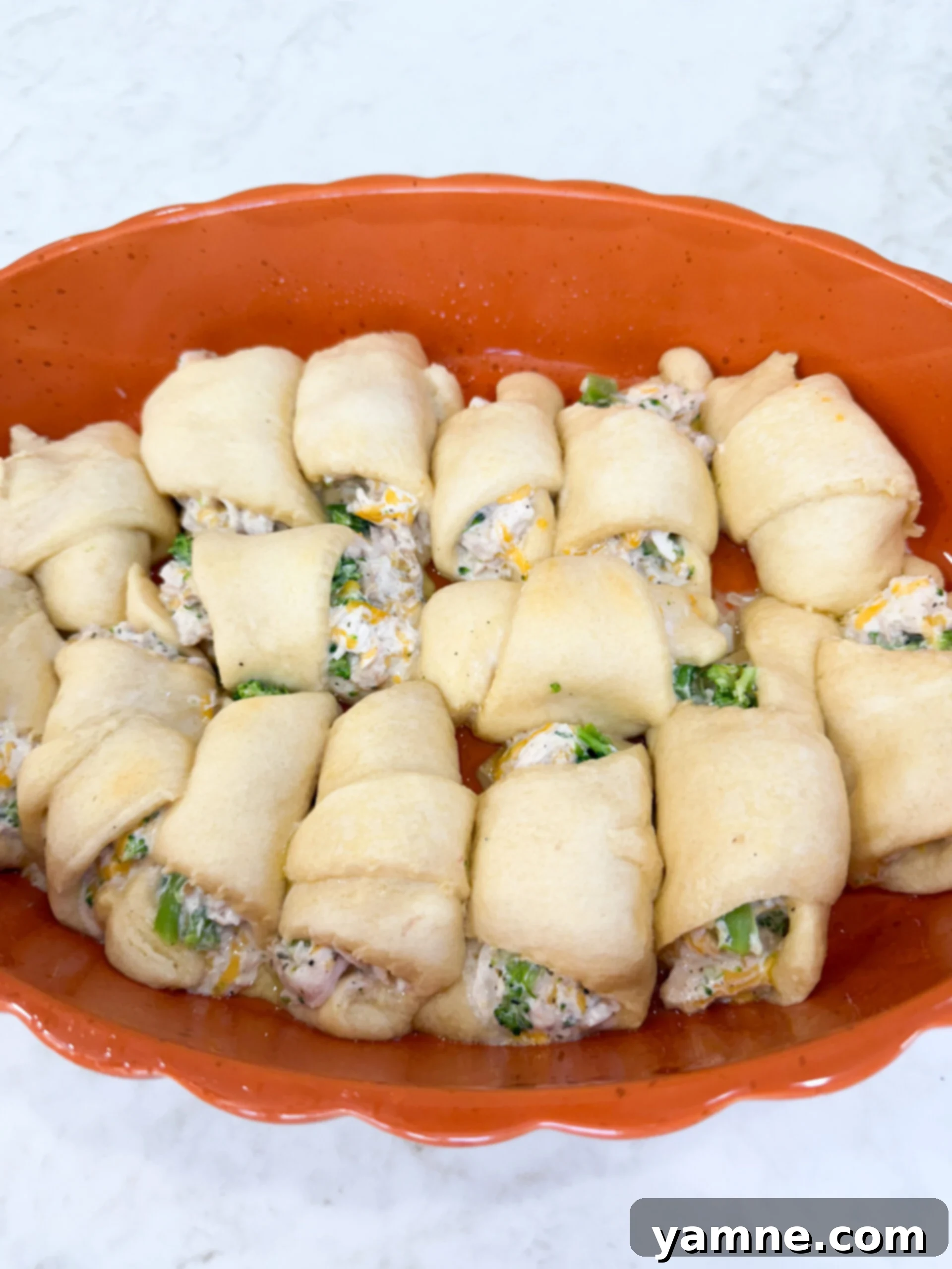 Flaky Cheesy Chicken and Broccoli Bake 7 Chicken and broccoli crescent rolls arranged neatly in a greased 9x13 inch baking pan, ready for the first bake.