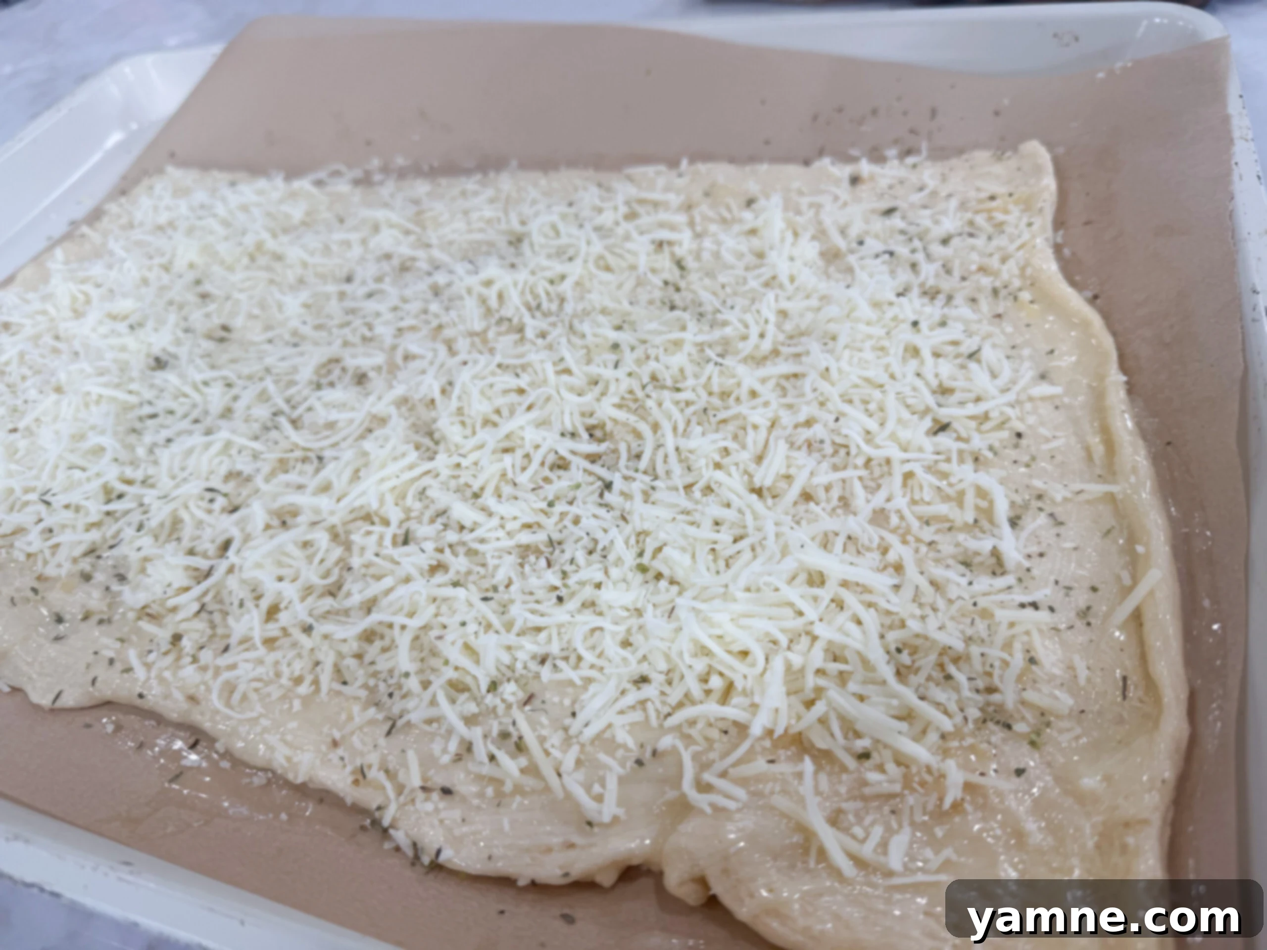 Sprinkling mozzarella and Parmesan cheese over dough