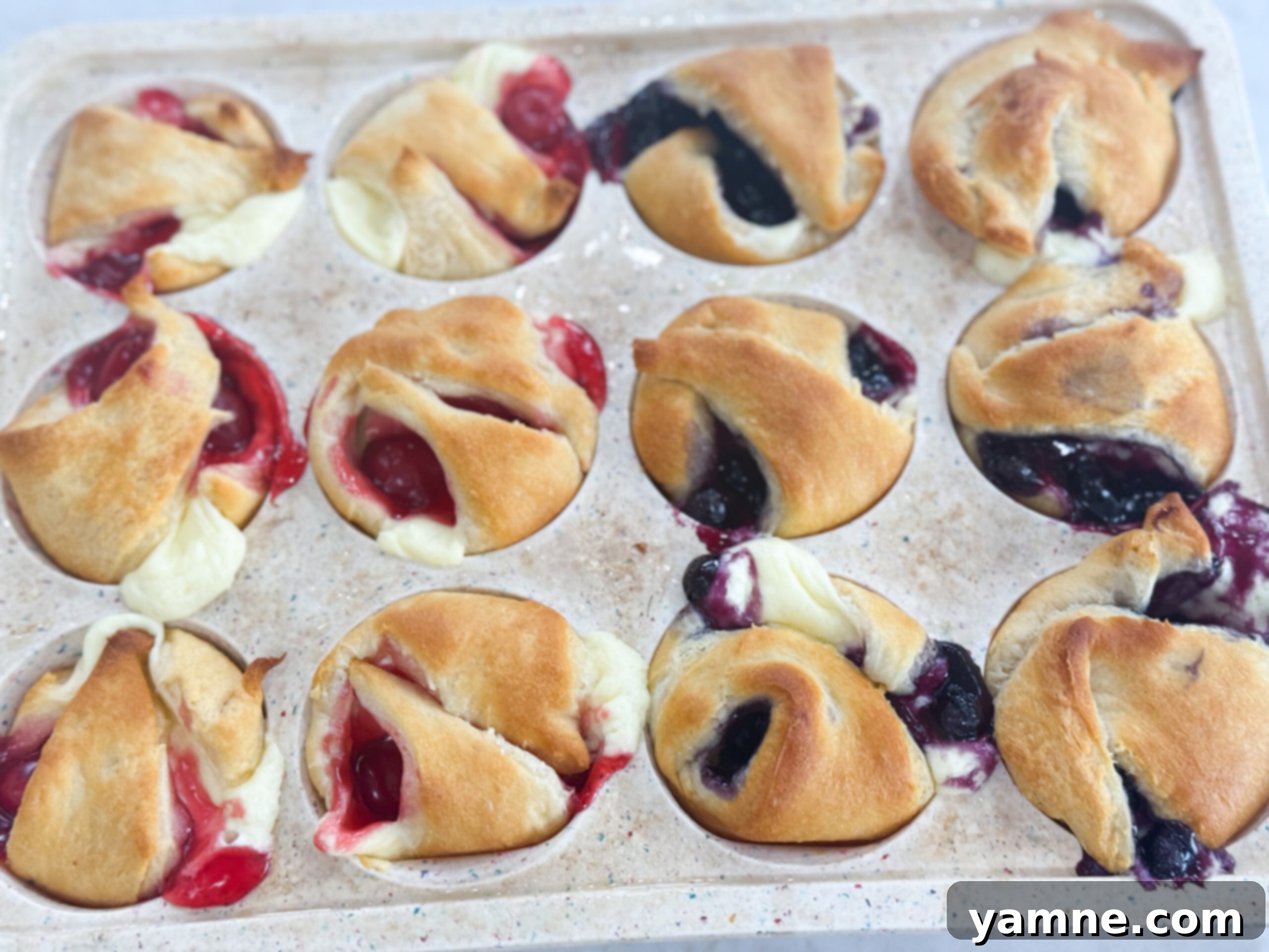 A batch of golden-brown mini cheesecake pies, fresh out of the oven, with glistening fruit filling on top.