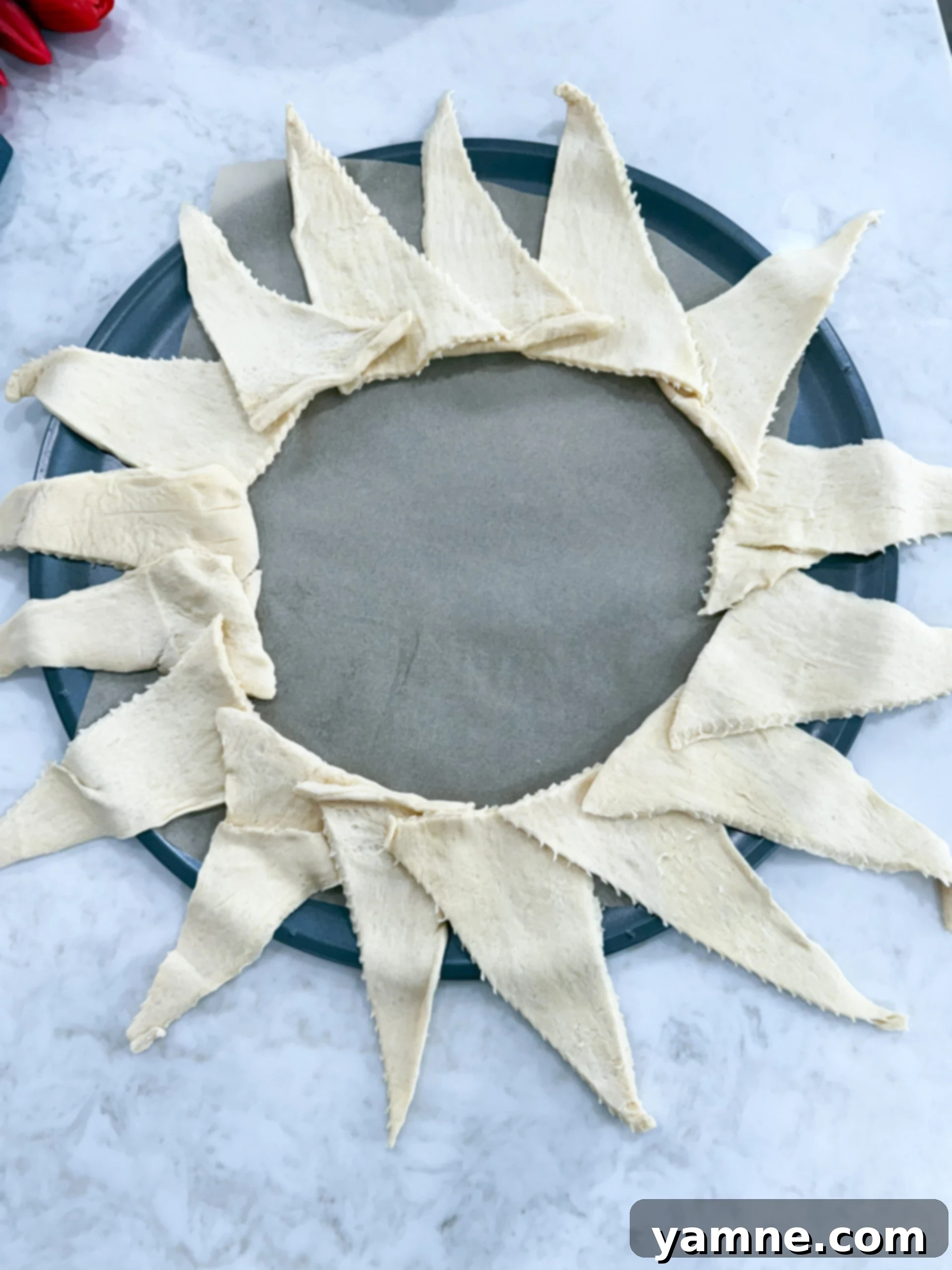 The chicken Alfredo filling being carefully added onto the prepared crescent dough ring base on a baking sheet.