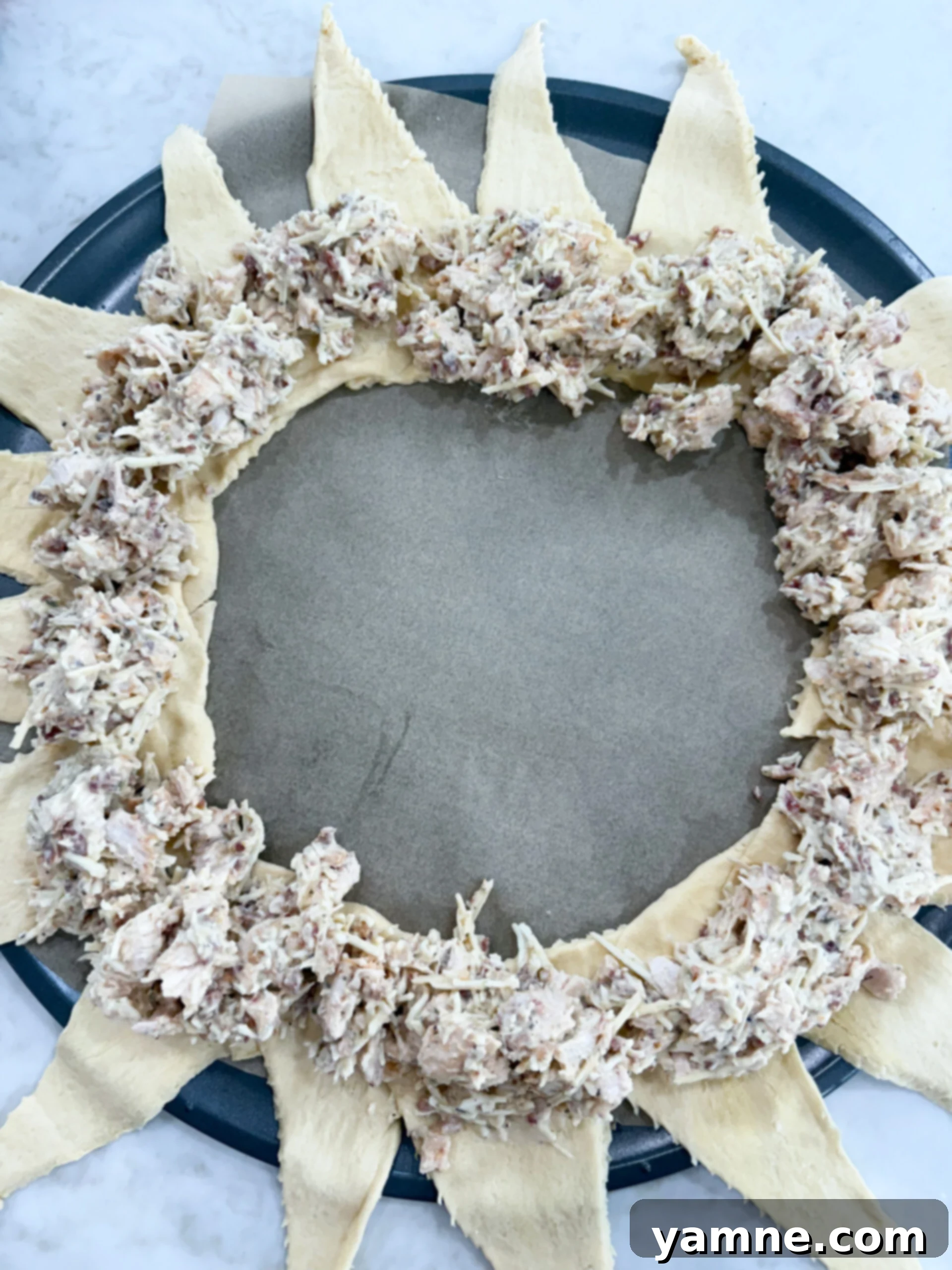 The chicken filling is evenly distributed around the circular crescent dough base, covering the overlapped wide ends.