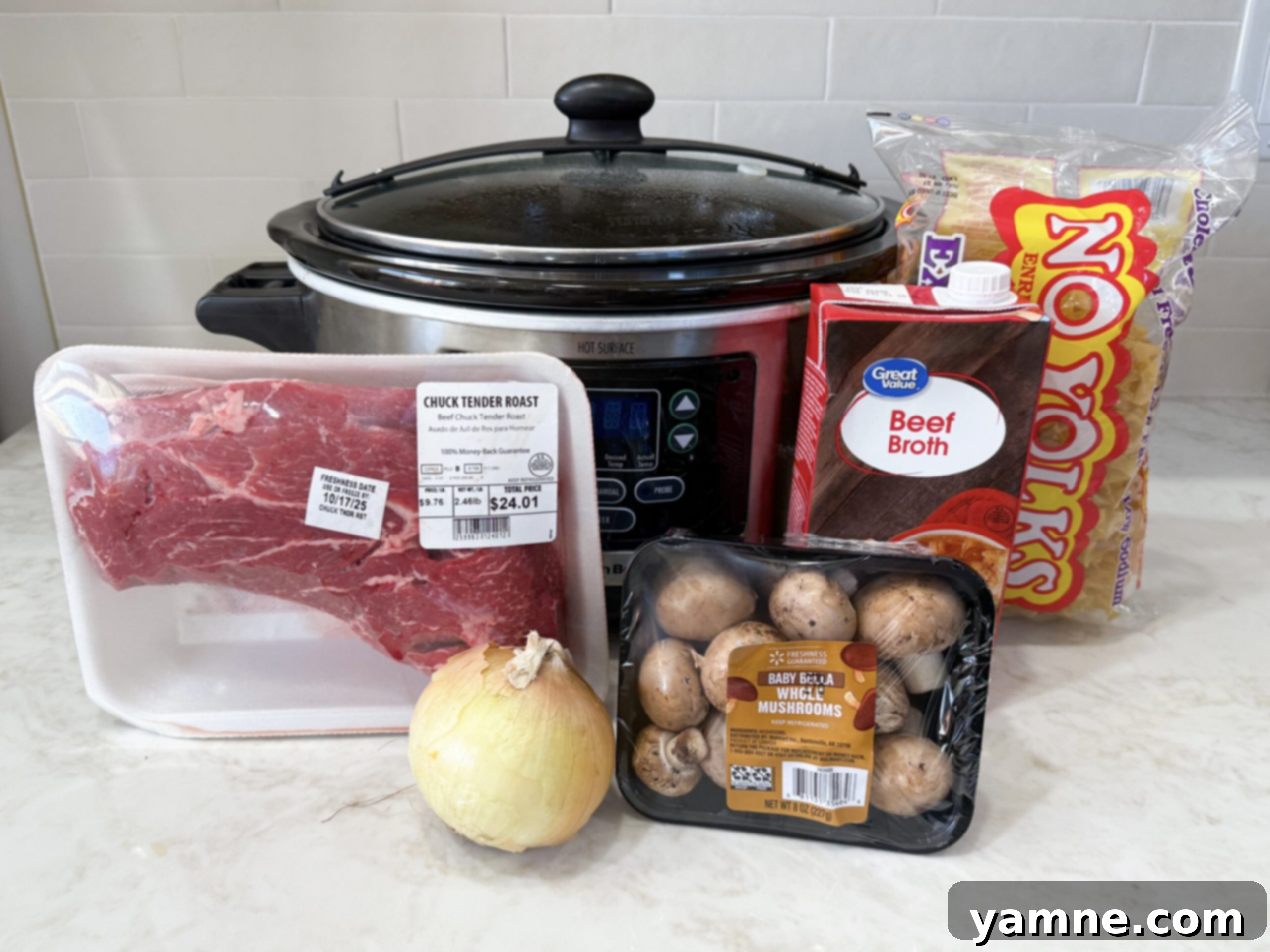 Easy Slow Cooker Beef Stroganoff 5 A collection of fresh ingredients laid out on a kitchen counter, including a chuck roast, whole brown mushrooms, an onion, beef broth, and a tub of sour cream, ready for making slow cooker beef stroganoff.