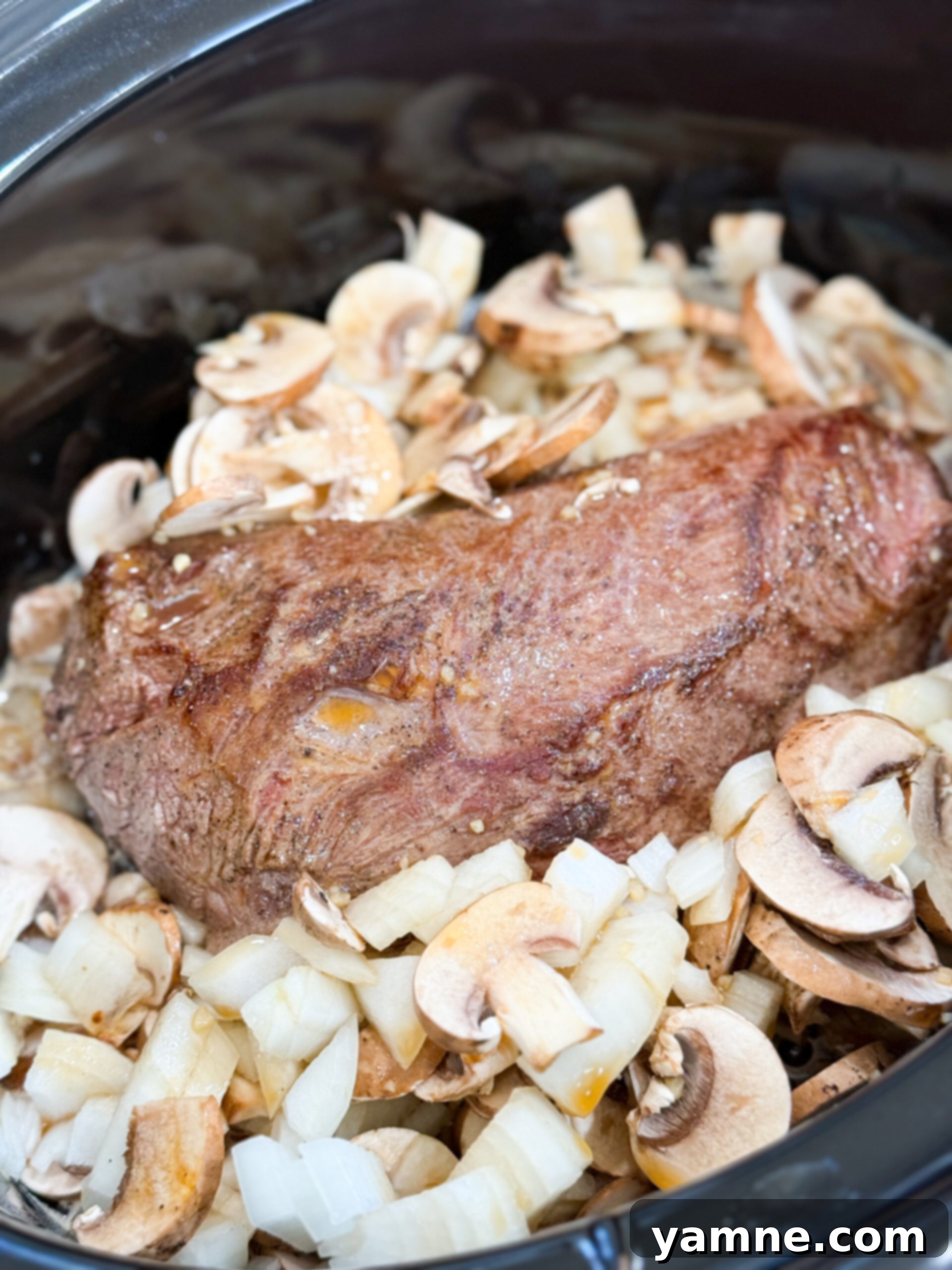 Easy Slow Cooker Beef Stroganoff 8 Diced onions and sliced mushrooms added around a seared beef roast in the slow cooker, with the broth mixture poured over.