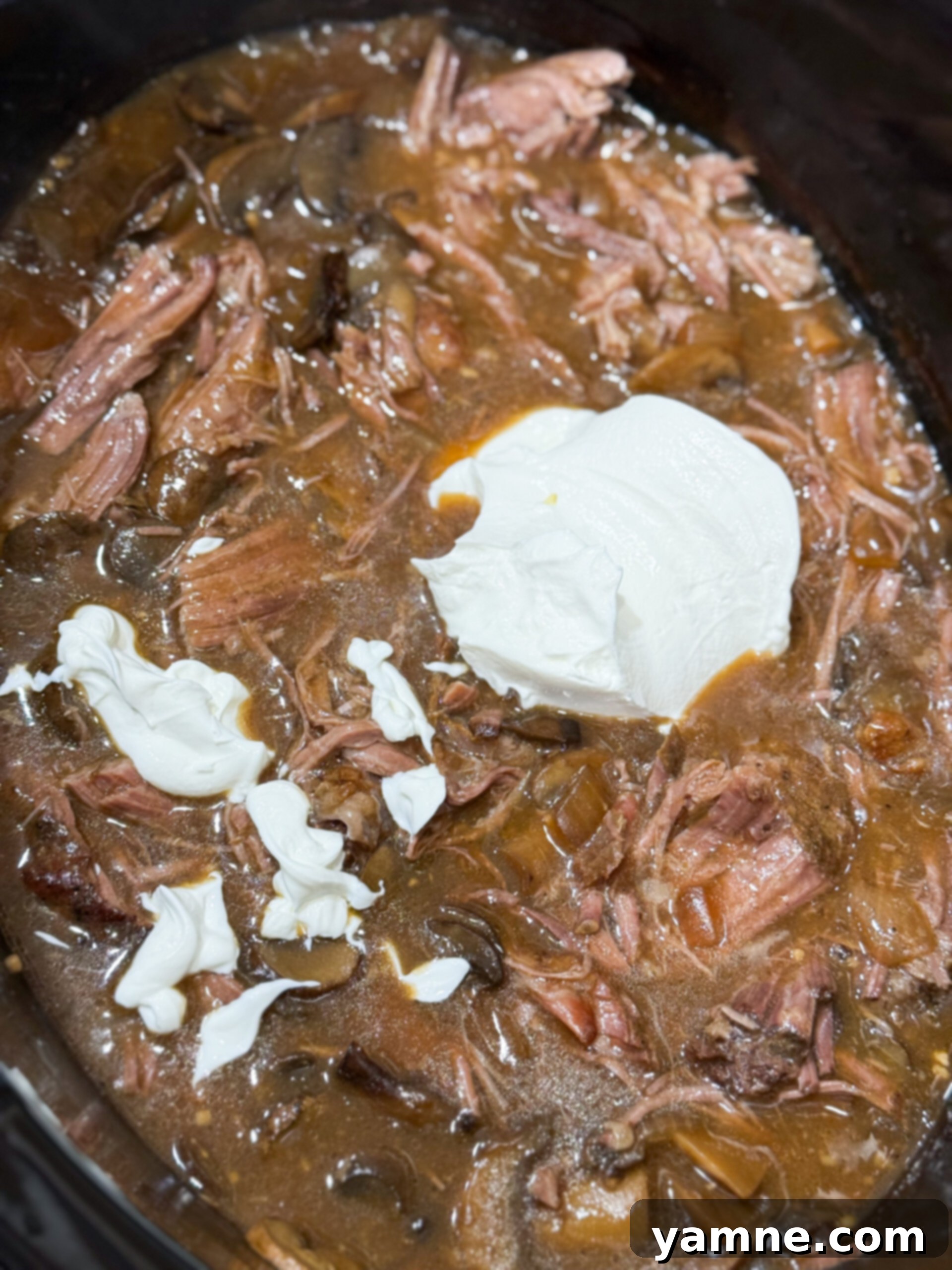 Easy Slow Cooker Beef Stroganoff 10 Sour cream being stirred into the finished beef stroganoff in the slow cooker, making the sauce creamy.
