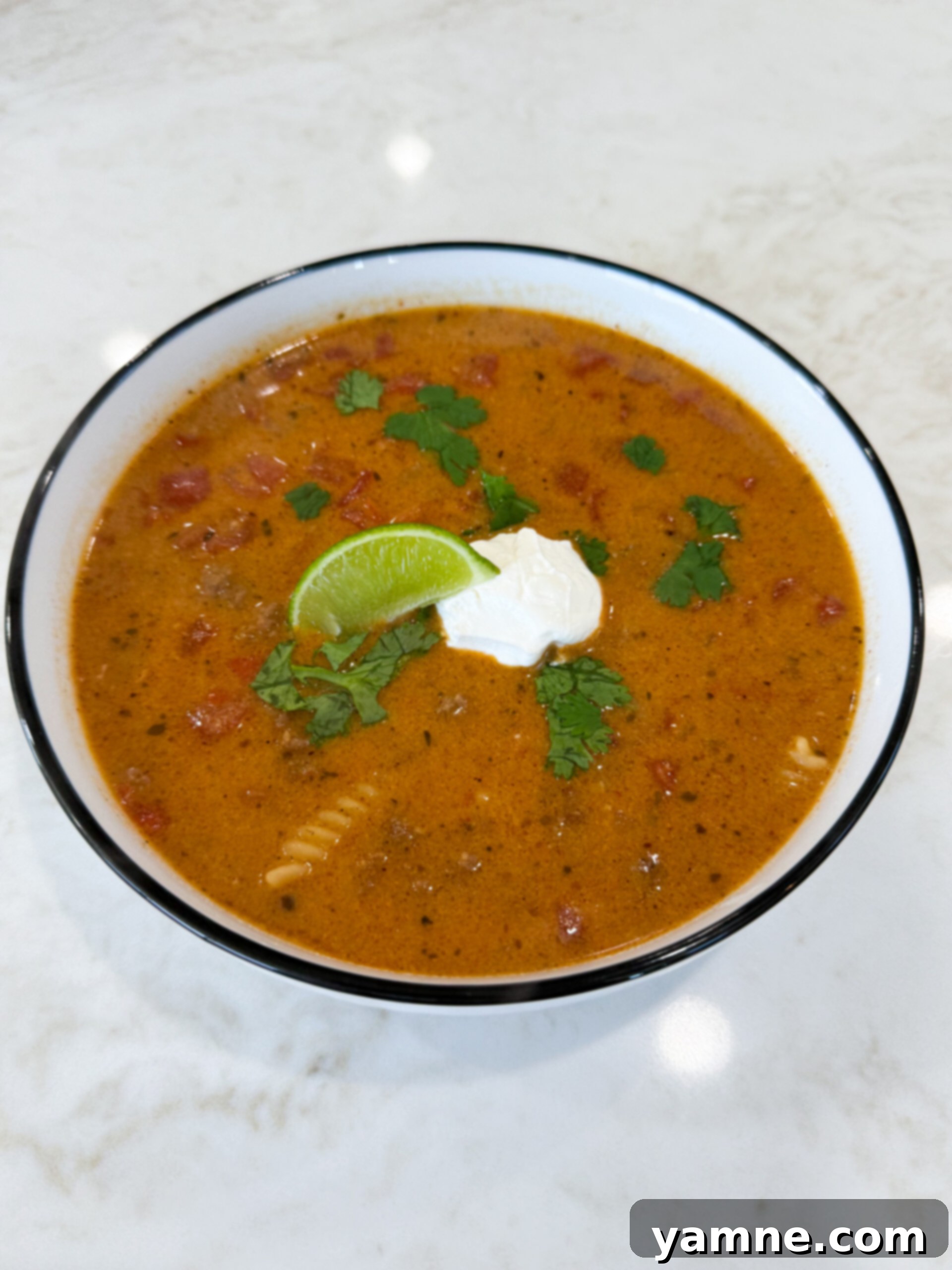 Bowl of cheesy queso chili topped with sour cream, lime, and cilantro