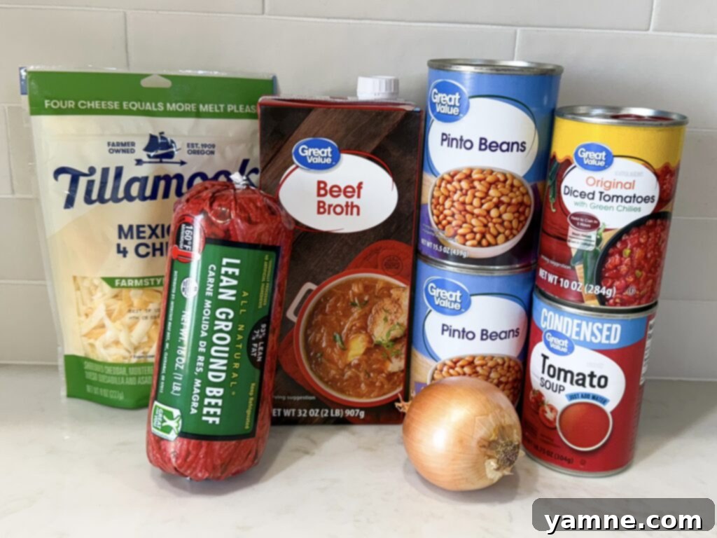 Ingredients for queso chili on counter including ground beef, beans, pasta, and cheese