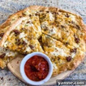 Close-up of a homemade breakfast pizza featuring a golden crescent roll crust, crumbled sausage, hash browns, fluffy scrambled eggs, and melted cheddar and parmesan cheese.