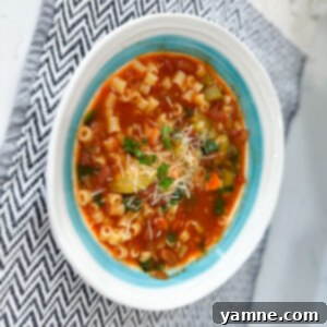 A steaming bowl of classic Minestrone soup, garnished with fresh herbs and a sprinkle of Parmesan cheese.