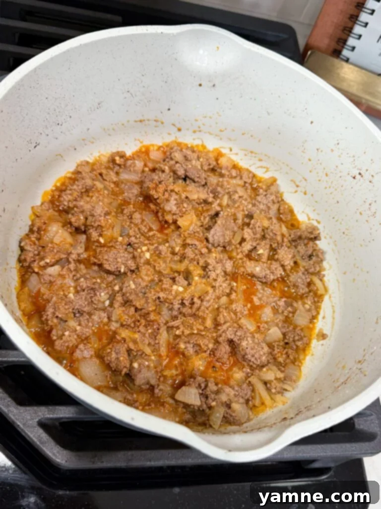 Browned ground beef and onions seasoned with paprika in a large skillet on the stovetop, ready for the broth.