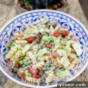 A colorful bowl of Summer Pasta Salad with rotini, peas, tomatoes, and bacon, tossed in a creamy dressing.