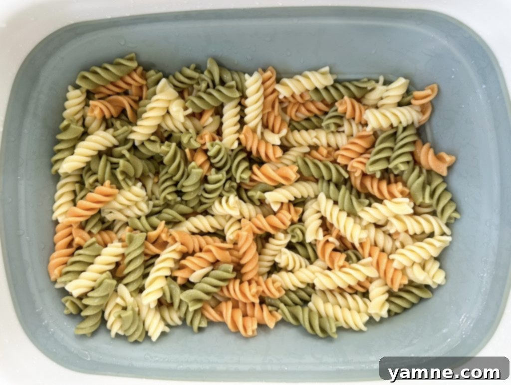 Cooked rotini pasta being rinsed with cold water in a colander, ready for ranch bacon pasta salad preparation.