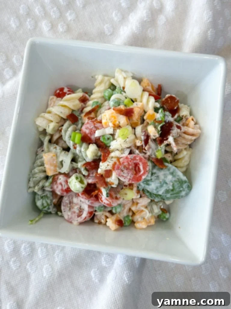 A close-up shot of creamy ranch bacon pasta salad, highlighting its texture and fresh ingredients, with a focus on cheese and bacon.
