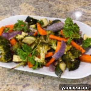 A vibrant platter of perfectly roasted zucchini, carrots, broccoli, and red onion, seasoned with herbs.