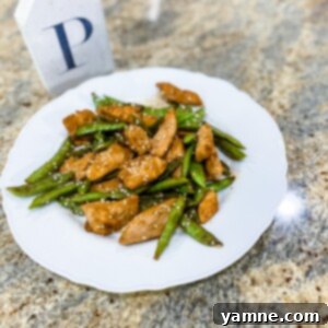 A close-up of Sticky Honey Garlic Chicken with vibrant sugar snap peas, garnished with fresh herbs, served on a modern plate.