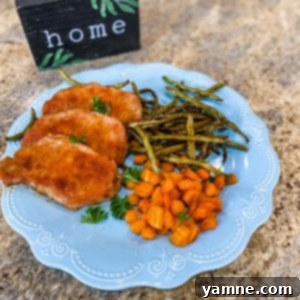 A perfectly cooked smokie pork chop served alongside roasted baby carrots and green beans on a parchment-lined sheet pan.