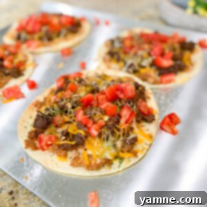 Crispy Taco Pizzas with seasoned ground beef, melted cheese, and diced tomatoes on a round flour tortilla base.