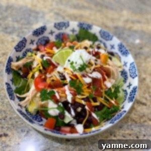 A vibrant and healthy Taco Chicken Power Bowl with seasoned chicken, black beans, lettuce, tomatoes, cheese, sour cream, salsa, and ranch.