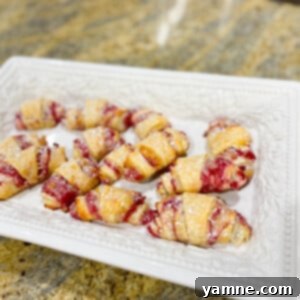 Raspberry Cream Cheese Delights 2 Golden-brown Raspberry Cream Cheese Roll-Ups with a dusting of powdered sugar, showcasing their flaky crust and delicious filling.