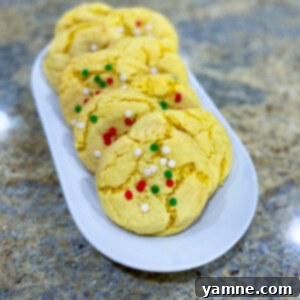 Easy Cake Mix Christmas Cookies 2 Festive Cake Mix Christmas Cookies adorned with colorful red and green sprinkles on a baking sheet, ready for holiday celebrations.