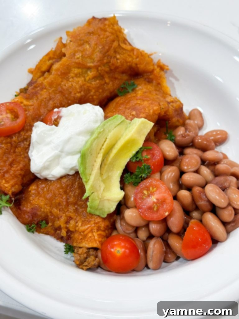 A serving of cheesy ground beef enchiladas on a plate, garnished with fresh cilantro and a dollop of sour cream.