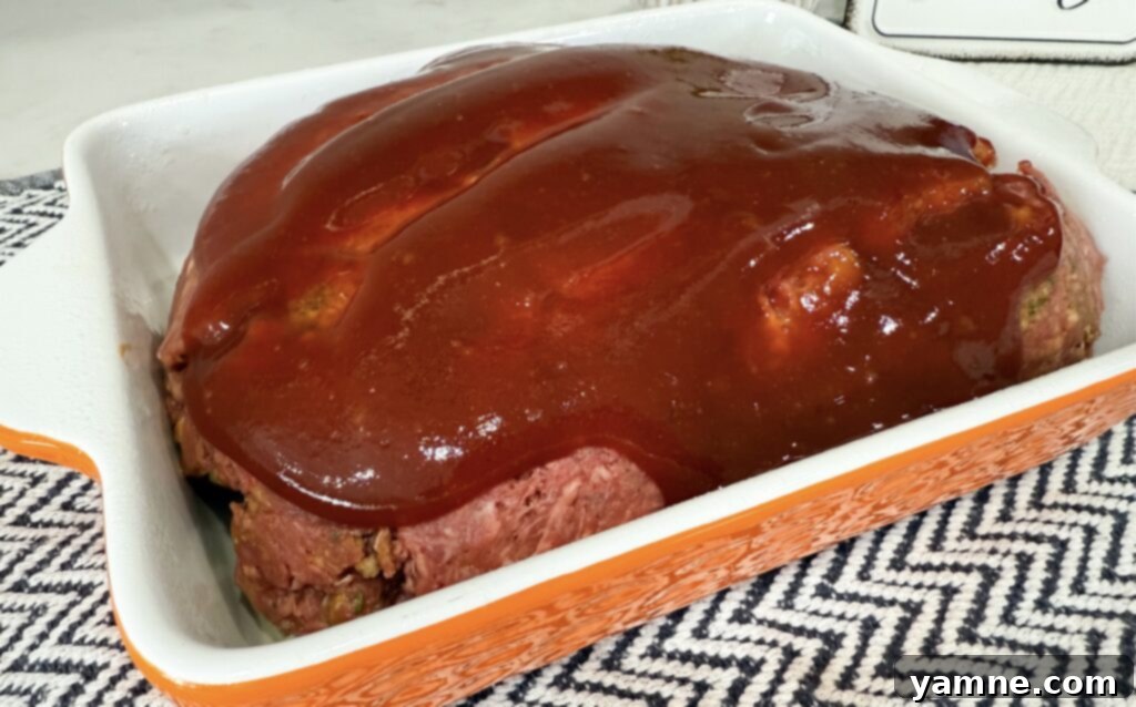 Shaping the meatloaf mixture into a loaf in the pan and spreading the glaze