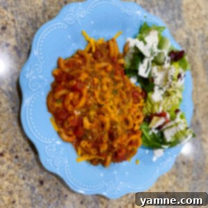 A delicious bowl of Old-Fashioned American Goulash with ground beef, macaroni, and tomato sauce, garnished with shredded cheddar cheese.